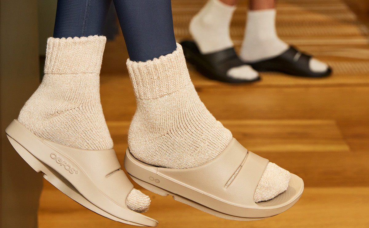 Close-up of feet wearing beige open-toe shoes with white socks on a wooden floor.