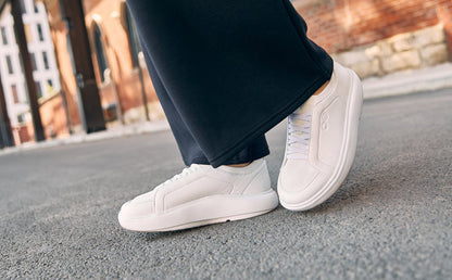 White sneakers worn on a person's feet with a blurred background | lifestyle