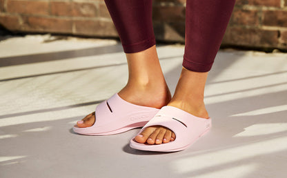 Person wearing pink slides on a concrete surface with a brick wall in the background | lifestyle