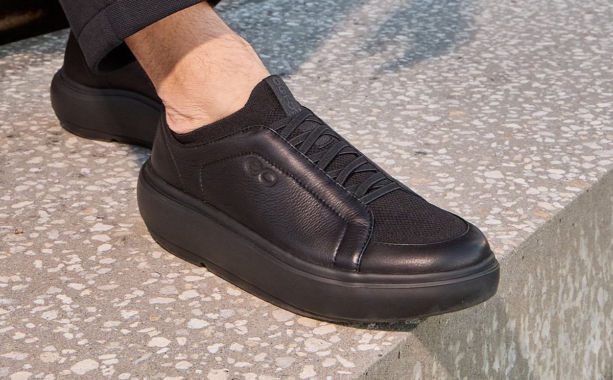 Black slip-on sneakers worn on a textured pavement surface | lifestyle