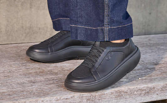 Black sneakers worn with blue jeans on a wooden floor | lifestyle
