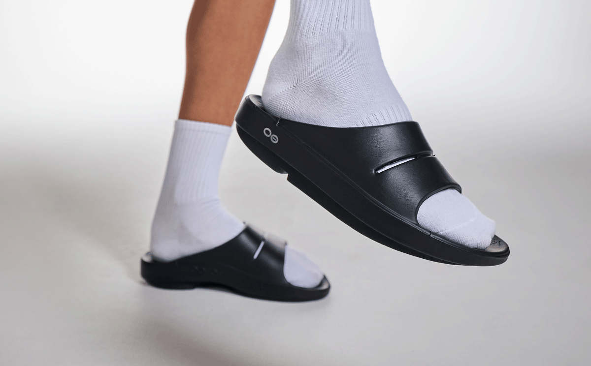 Women's OOahh Slide Sandal - Black close up of shoe on model lifting foot up in studio | lifestyle
