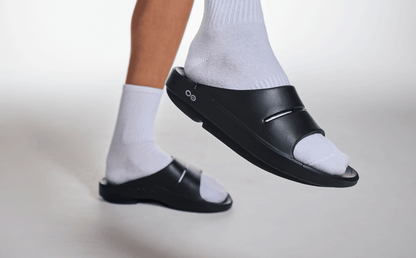 Women's OOahh Slide Sandal - Black close up of shoe on model lifting foot up in studio | lifestyle