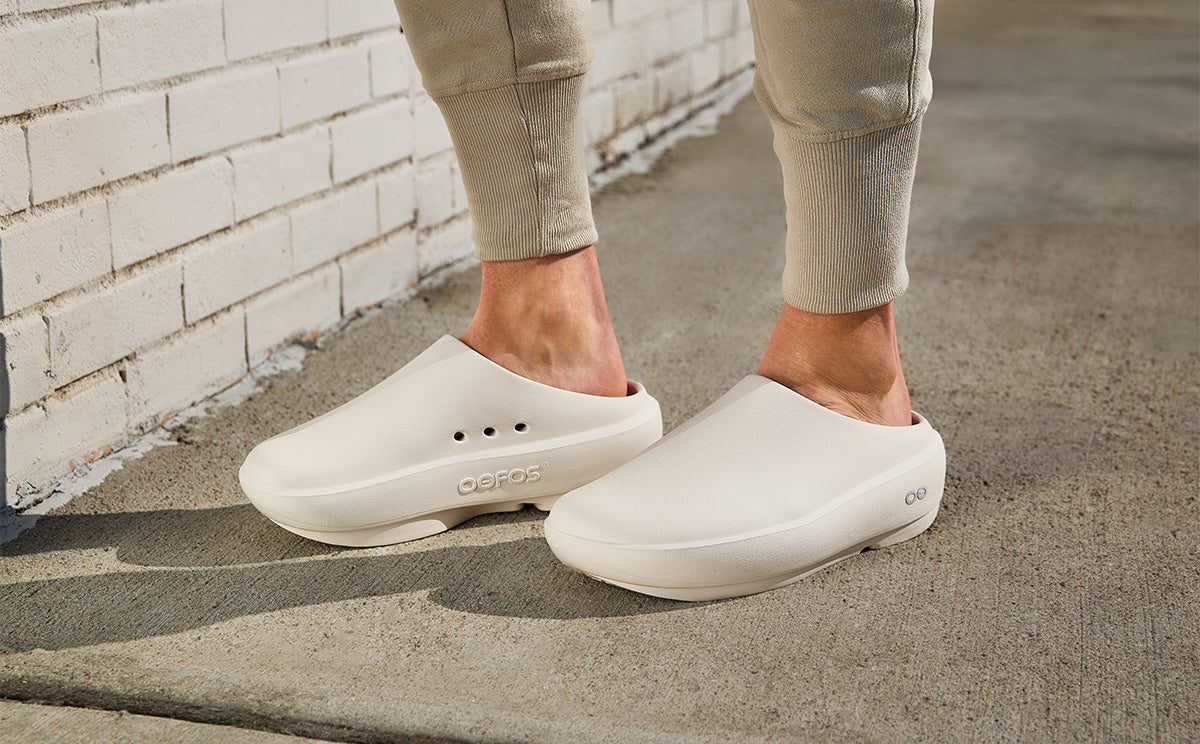 Person wearing chalk clogs on a concrete surface with a brick wall in the background