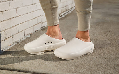 Person wearing chalk clogs on a concrete surface with a brick wall in the background