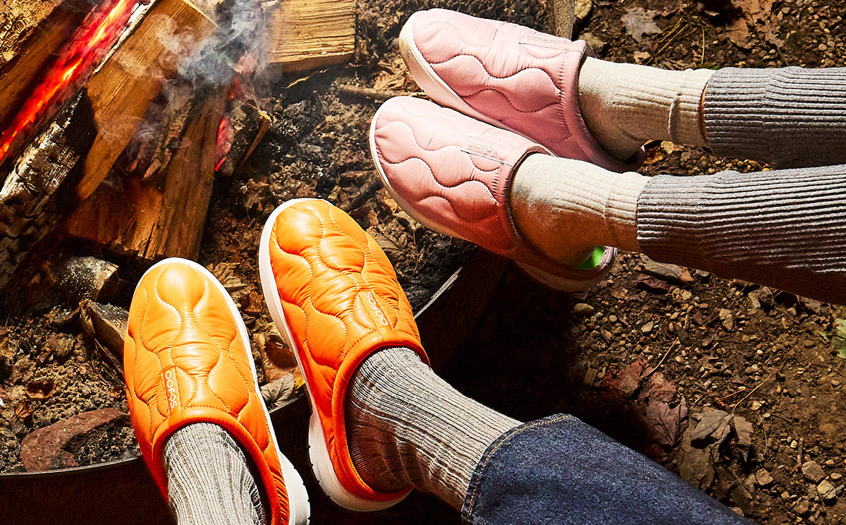 Person wearing orange shoes and gray socks by a fire
