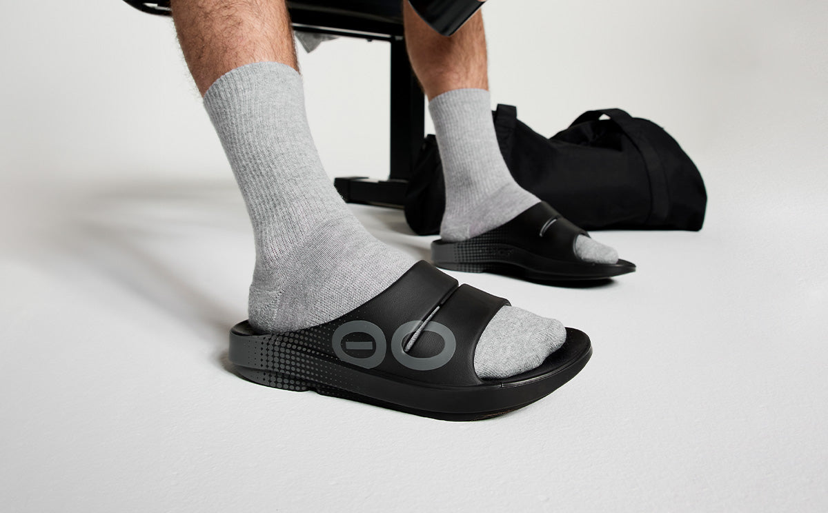 Men's OOahh Sport Slide Sandal - Black Matrix model sitting on bench in studio | lifestyle