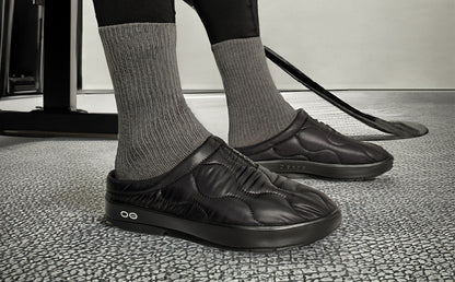 Men's OOcoozie Thermo Mule - Black model standing inside wearing shoes with hockey stick next to him | lifestyle