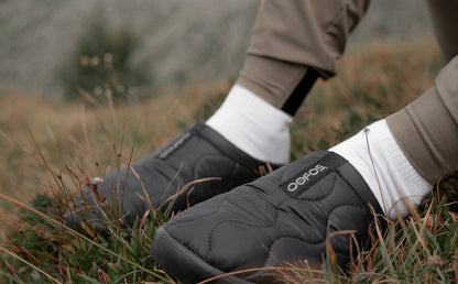 Men's OOcoozie Thermo Mule - Black model sitting outside in grass wearing shoes | lifestyle