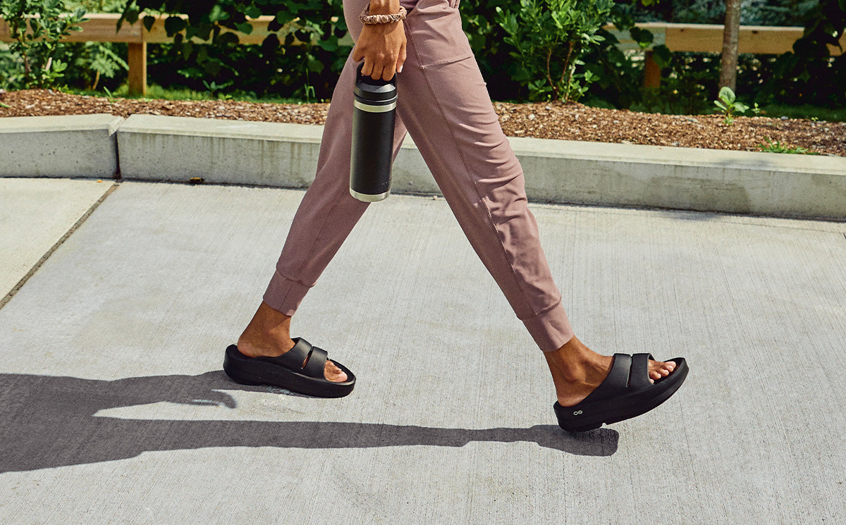 Women's OOmega OOahh Sandal - Black lifestyle side view image of model walking in shoes | lifestyle