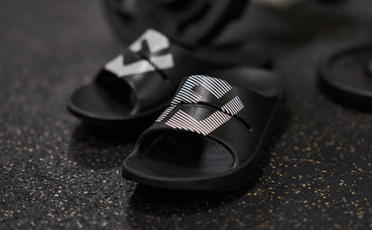 FJ X OOFOS Men's OOahh Sport Slide Sandal - Black close up of shoes on gym floor | lifestyle