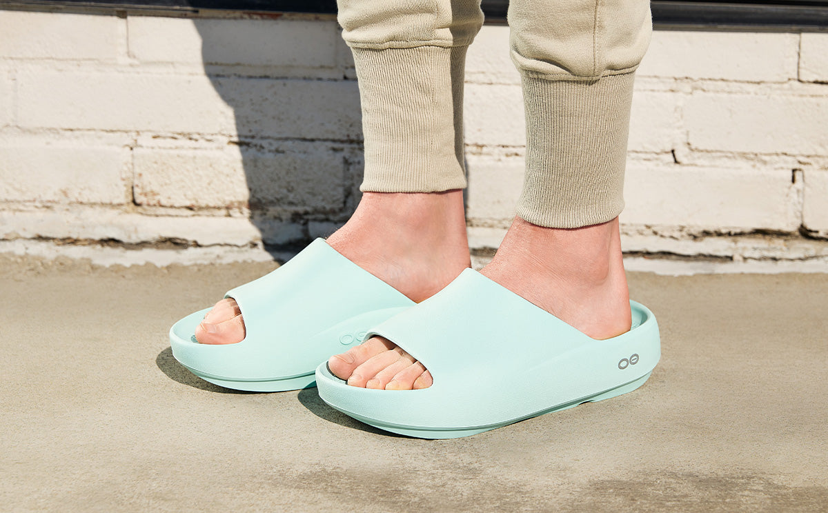 Person wearing light blue sandals on a concrete surface with a stone wall background | lifestyle