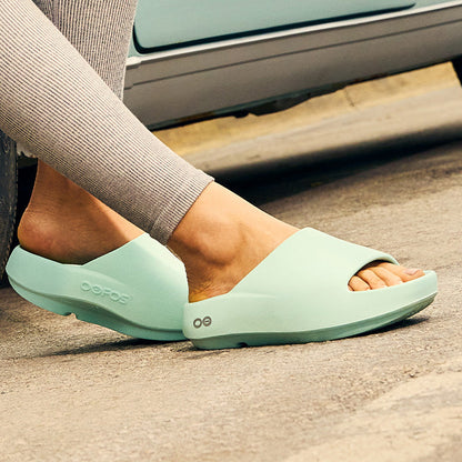 Person wearing light green sandals on a street with a car and motorcycle in the background | lifestyle