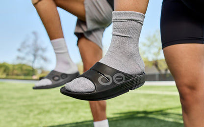 Women's OOahh Sport Slide Sandal - Black Matrix models outside with leg up wearing black matrix and slate matrix | lifestyle