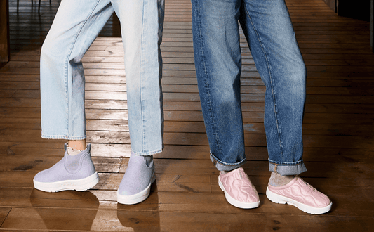 Two pairs of legs wearing light blue jeans and sneakers on a wooden floor.