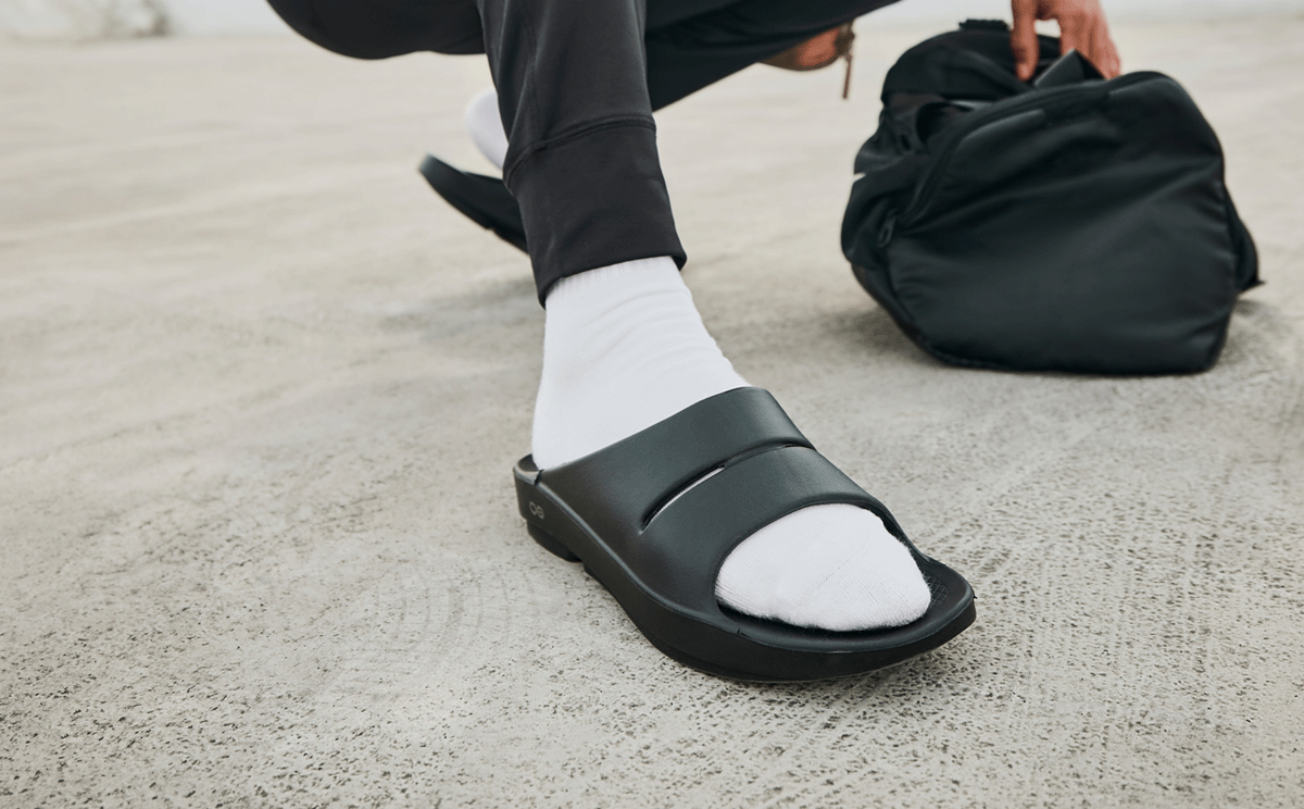 Men's OOahh Slide Sandal - Black close up of shoe on model crouching outside | lifestyle