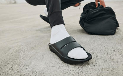 Men's OOahh Slide Sandal - Black close up of shoe on model crouching outside | lifestyle
